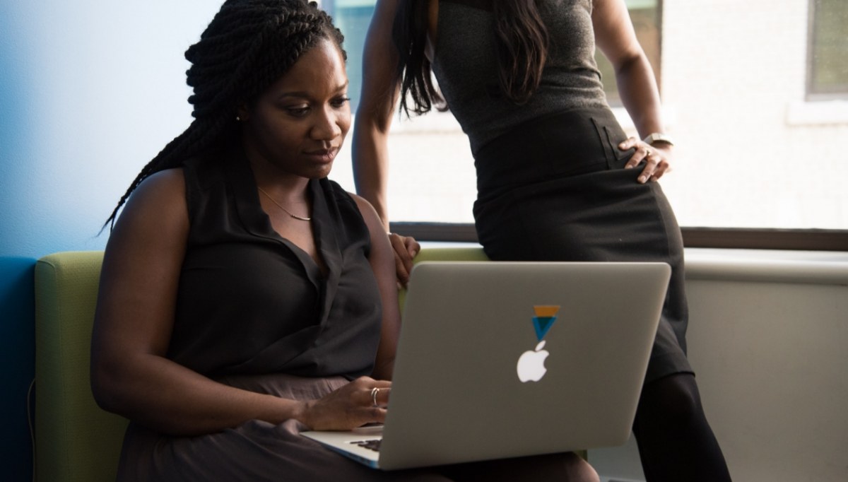 A black woman sitting on a couch with an open apple computer on her lap.