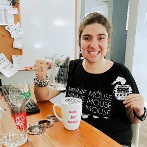 Smiling woman holding up a printed glass. Other printed glasses and mugs are sitting on the table in front of her.