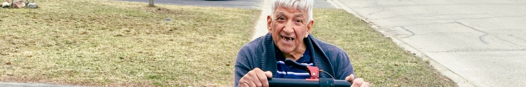 An elderly grey haired man riding on a scooter.