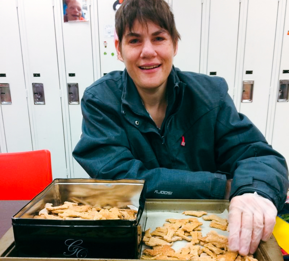 A short haired woman in a dark shirt taking baked dog cookies off a tray and putting them in a black tin.