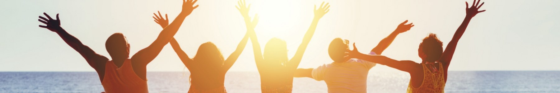 Five young adults in front of a lake with their arms stretched above their heads. The sun is setting in the background.