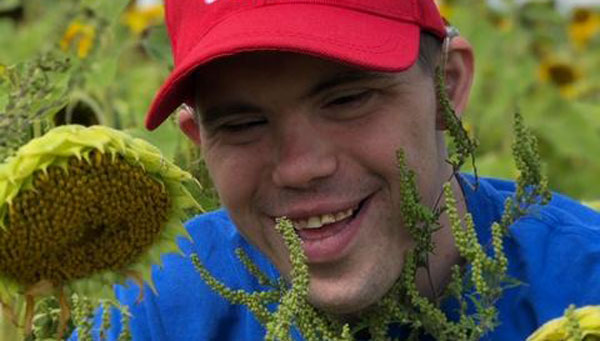 Close up of a smiling young man and a sunflower .