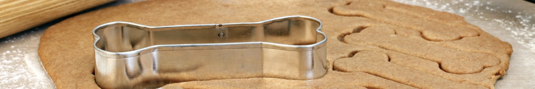Dough rolled out on a table with dog bone shaped cookies cut and the cutter on top.